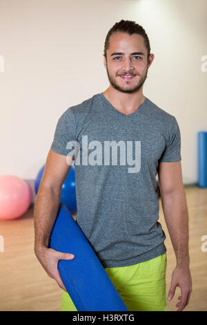 Portrait of smiling man holding rolled exercise mat Stock Photo