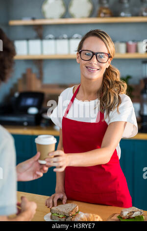 Smiling waitress serving a coffee to customer at counter in cafÃ© Stock Photo