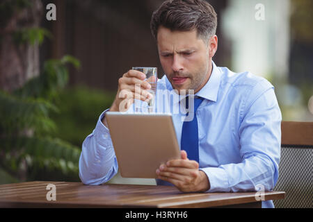 Businessman having drink while using digital tablet Stock Photo