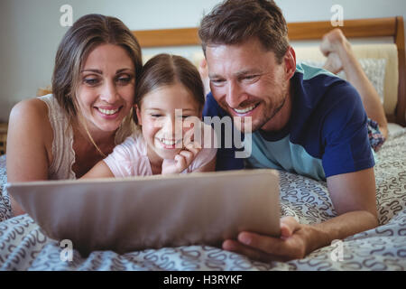 Parents lying with daughter on bed and using laptop Stock Photo