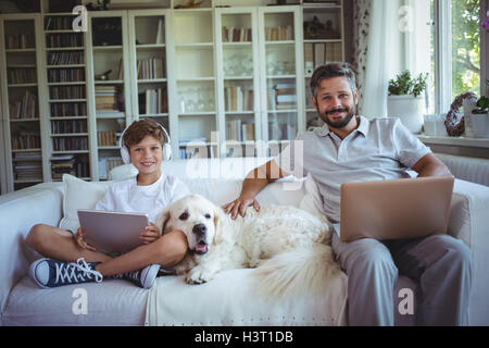 Father and son sitting on sofa and using digital tablet and laptop Stock Photo