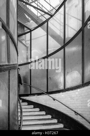 Black and white image of a man appearing around the curve as he descends the entrance steps of the Greenwich Foot Tunnel, London, UK Stock Photo