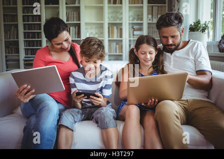 Happy family sitting on sofa and using laptop, mobile phone and digital tablet Stock Photo