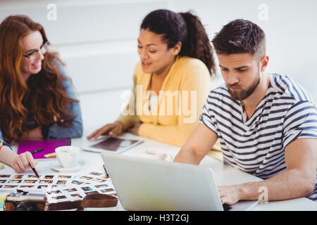 Editor using laptop with colleagues talking at creative office Stock Photo