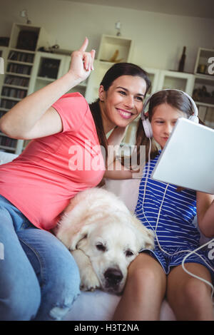 Happy mother and daughter sitting with pet dog and using digital Stock Photo
