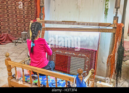 The young woman weave the traditional Uzbek rug at the workshop in Bukhara. Stock Photo