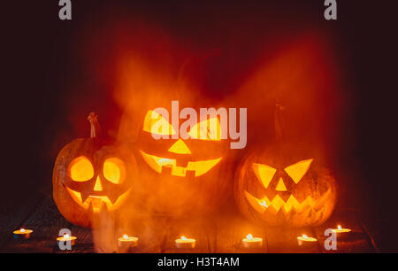 Three glowing pumpkins symbolizing the head of old Jack, with smoke on wooden background. Soft focus. shallow DOF Stock Photo