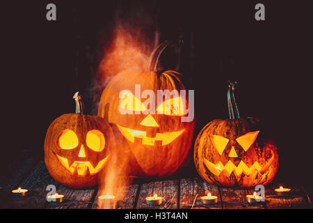 Three glowing pumpkins symbolizing the head of old Jack, with smoke on wooden background. Soft focus. shallow DOF Stock Photo