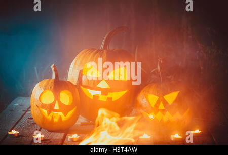 Three glowing pumpkins symbolizing the head of old Jack, with smoke on wooden background. Soft focus. shallow DOF Stock Photo