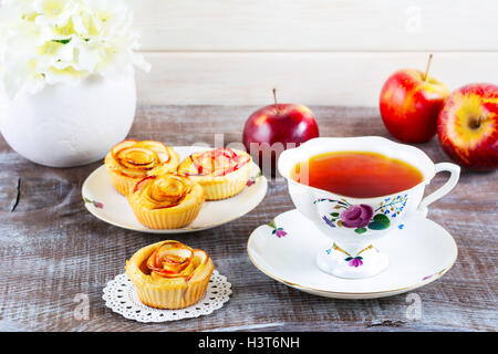 Cup of tea and muffins with rose shaped apple slices. Sweet apple dessert pie. Homemade apple rose pastry. Breakfast tea with sw Stock Photo