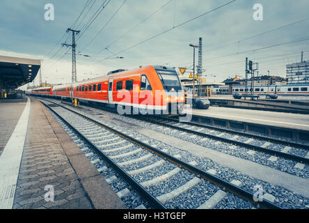 Beautiful railway station with modern high speed red commuter train at colorful sunset. Railroad with vintage toning. Train Stock Photo