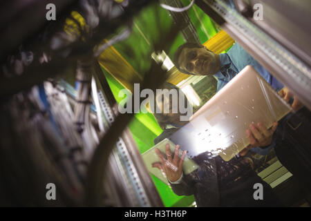 Technicians using digital tablet and laptop while analyzing server Stock Photo