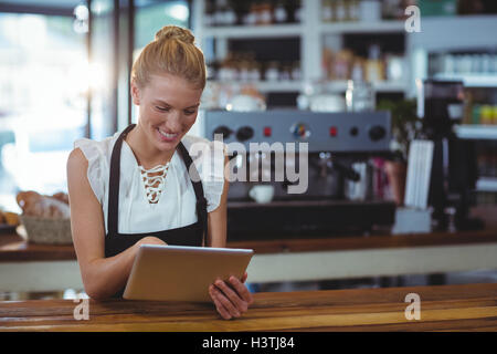 Smiling waitress standing at counter using digital tablet Stock Photo