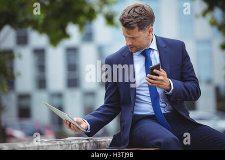 Handsome businessman holding mobile phone while using digital tablet Stock Photo