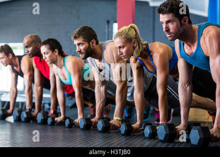 People doing push-ups with dumbbell in gym Stock Photo