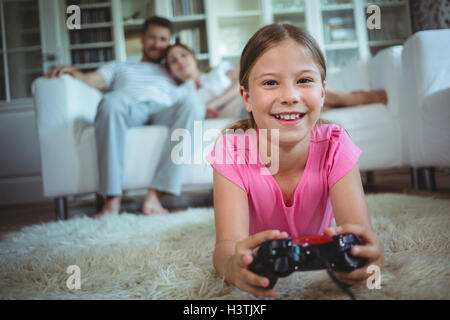 Smiling girl lying on rug and playing video game in living room Stock Photo