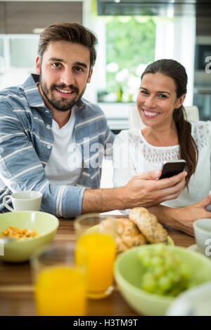 Couple using mobile phone while having breakfast at home Stock Photo