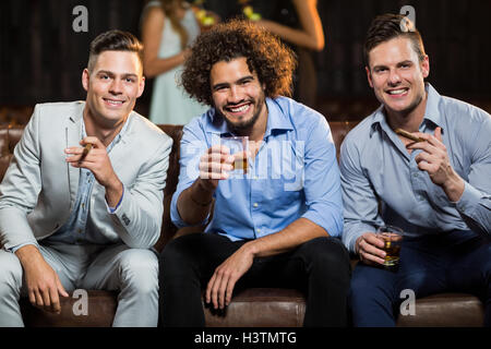 Three happy friends having cigar and whisky in bar Stock Photo