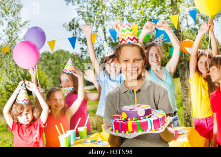 Happy young boy in party hat holding birthday cake Stock Photo