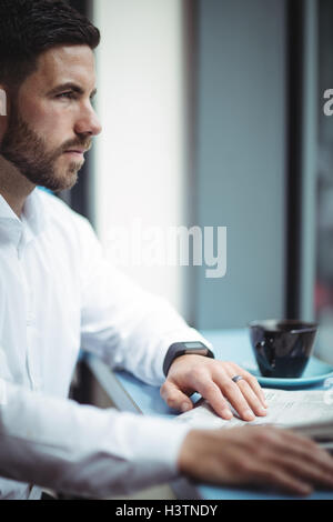 Businessman sitting at table and reading newspaper in office Stock Photo
