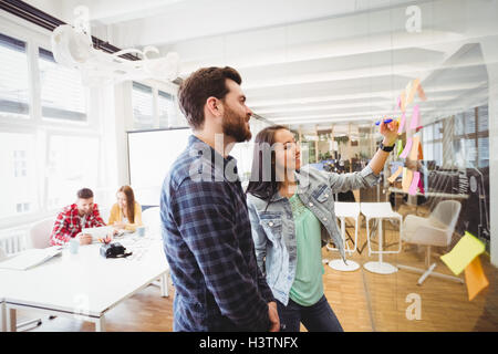 Smiling business people looking at multi colored sticky notes on glass Stock Photo