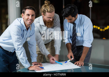 Businessman smiling at camera while colleagues discussing over blueprint Stock Photo
