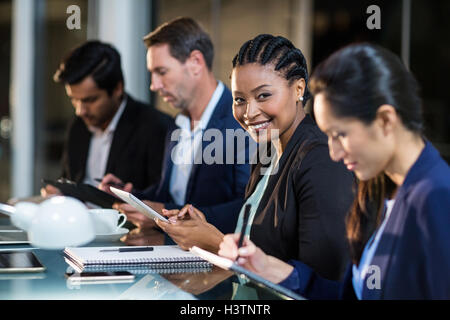 Businesswoman using digital tablet while colleagues writing notes Stock Photo