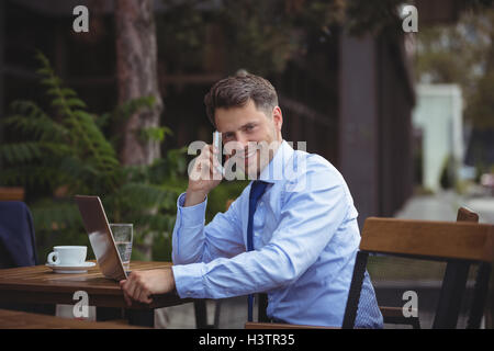 Handsome businessman talking on mobile phone while using laptop Stock Photo