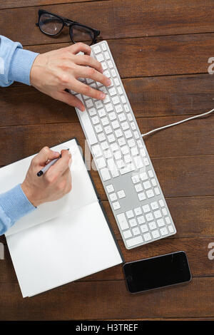 Man typing on keyboard and writing in diary Stock Photo