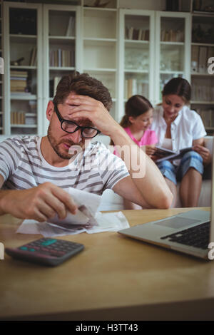 Worried man calculating bills while his wife and daughter sitting on sofa Stock Photo