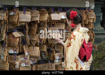 Woman dressed in traditional kimono looks at Ema wish plaques at Ueno Toshogu Shrine, Tokyo, Japan Stock Photo