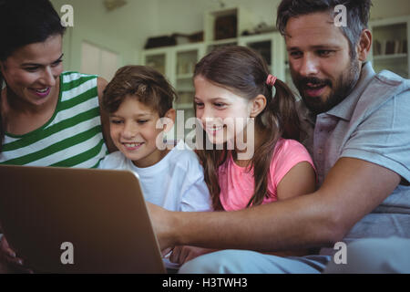 Parents sitting on sofa with their children and using laptop in living room Stock Photo