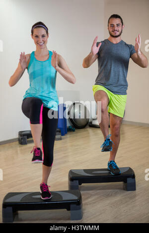 Smiling man and woman doing step aerobic exercise on stepper Stock Photo
