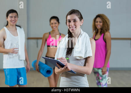 Portrait of female trainer holding clipboard with fitness class in background Stock Photo