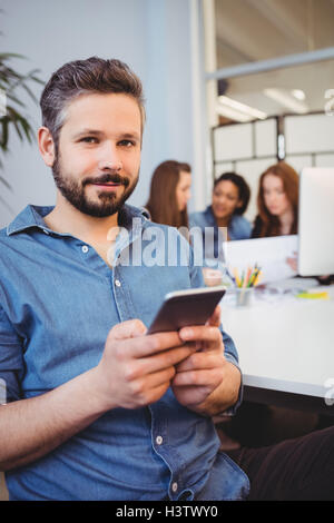 Portrait of businessman using mobile phone against coworkers Stock Photo