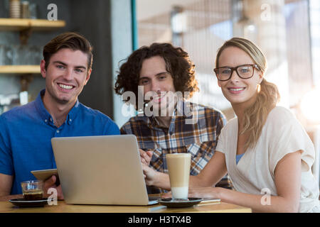 Smiling friends using digital tablet and laptop in caf├⌐ Stock Photo