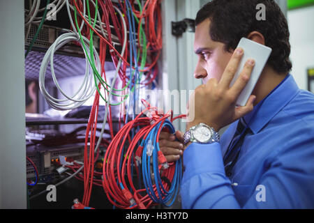 Technician talking on mobile phone while checking cables Stock Photo