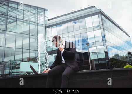 Businessman using laptop while talking on phone Stock Photo