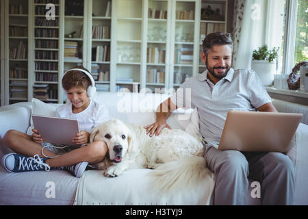 Father and son sitting on sofa and using digital tablet and laptop Stock Photo