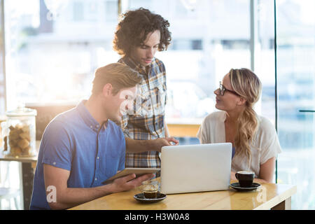 Friends using digital tablet and laptop in caf├⌐ Stock Photo
