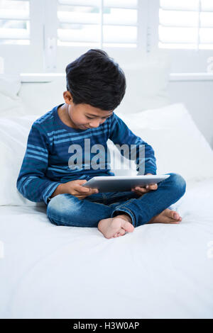 Boy using digital tablet while relaxing on bed Stock Photo