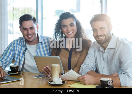 Smiling friends using digital tablet and laptop in caf├⌐ Stock Photo