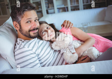 Smiling father and daughter sitting on sofa with a teddy bear Stock Photo