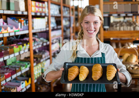 Smiling female staff holding tray of croissants in supermarket Stock Photo