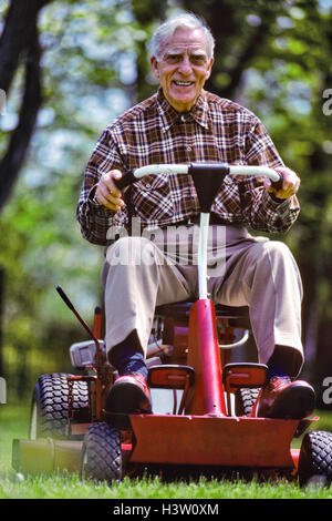 1980s SMILING OLDER MAN ON RIDING MOWER MOWING LAWN Stock Photo