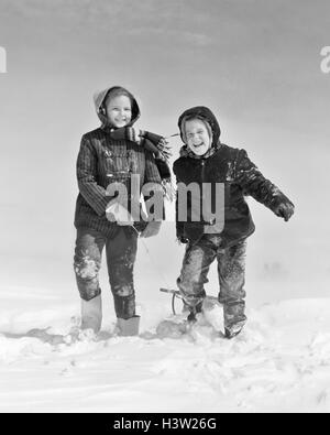 1950s 1960s SMILING BOY GIRL PULLING SLED IN WINTER SNOW Stock Photo