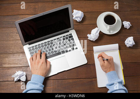 Man using laptop while writing on notepad Stock Photo