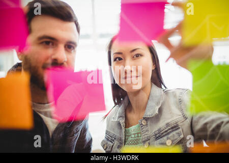 Business people looking at multi colored sticky notes on glass Stock Photo