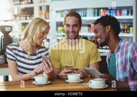 Three friends using mobile phones while having cup of coffee Stock Photo