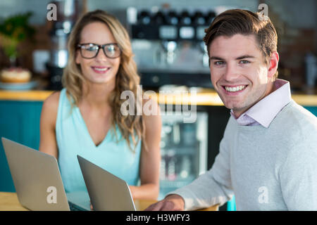 Smiling man and woman using laptop in cafe Stock Photo